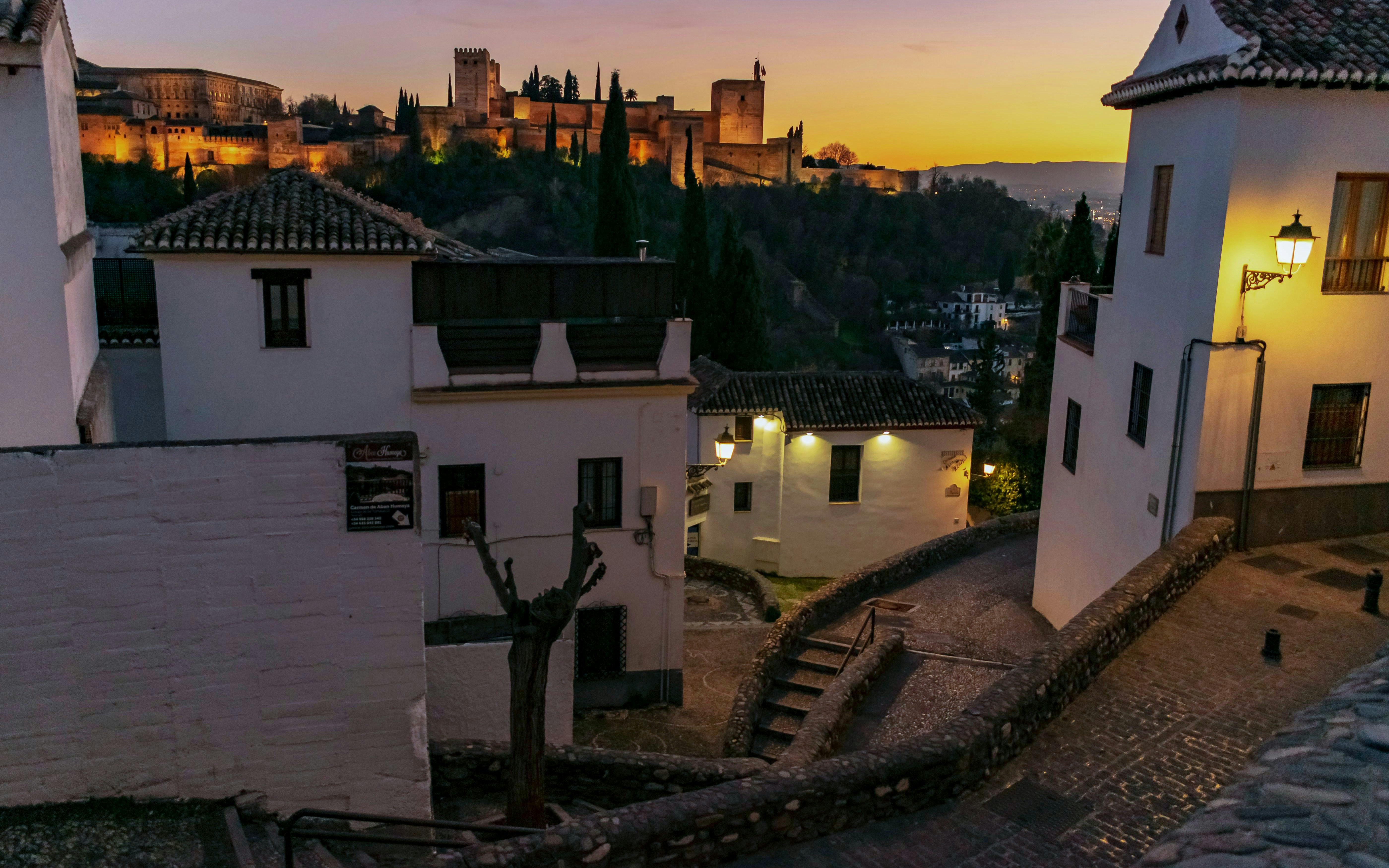 Panoramic view of the Alhambra at sunset from a cobblestone street in Granada.
