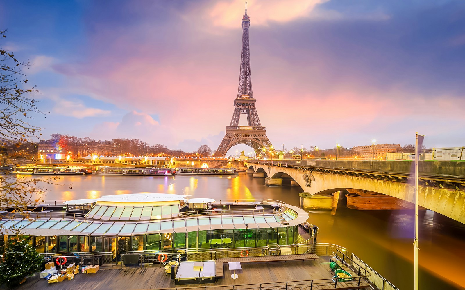 Eiffel Tower light show viewed from Seine River with boats and bridge in Paris.