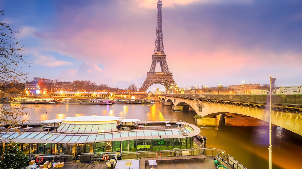 Eiffel Tower light show viewed from Seine River with boats and bridge in Paris.