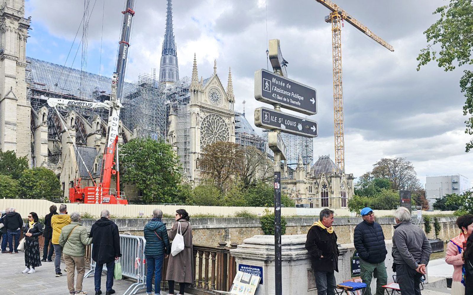 Notre Dame Cathedral under renovation with cranes and tourists in Paris.