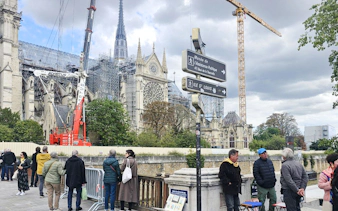 Notre Dame Cathedral under renovation with cranes and tourists in Paris.