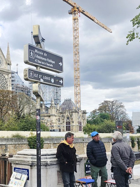 Notre Dame Cathedral under renovation with cranes and tourists in Paris.