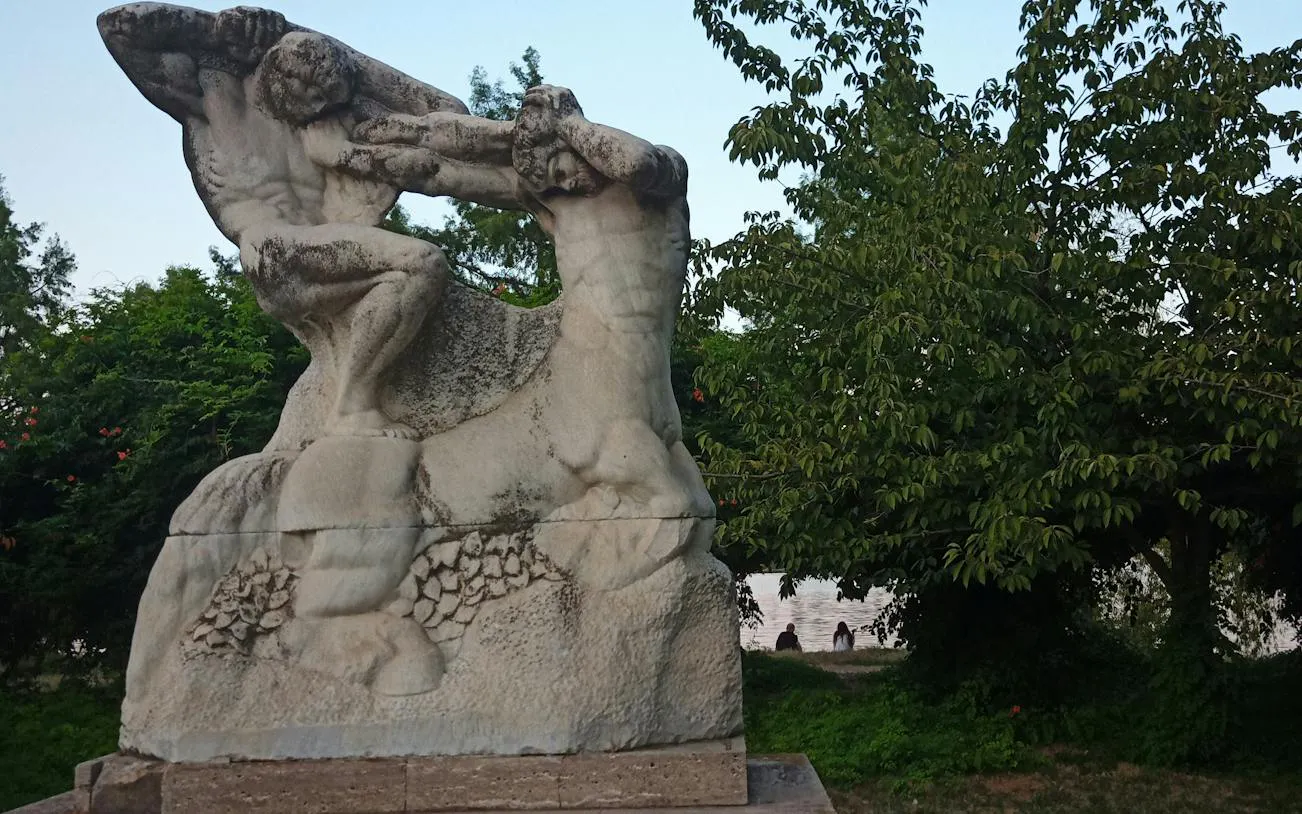 Stone sculpture in a park setting, part of the Romantic Bucharest self-guided city exploration game.