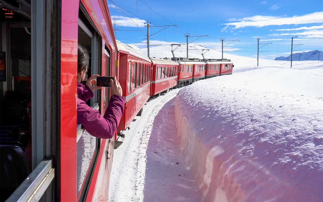 Passenger photographing snowy landscape from Bernina train window.