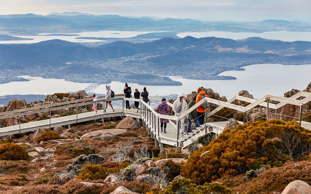 Visitors walking on Mt Wellington boardwalk with views of Hobart, Tasmania in the background.