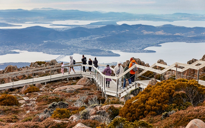 Visitors walking on Mt Wellington boardwalk with views of Hobart, Tasmania in the background.