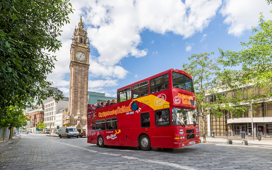 Red double-decker bus near Belfast's Albert Memorial Clock on sightseeing tour.
