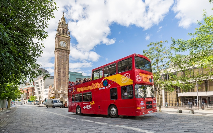 Red double-decker bus near Belfast's Albert Memorial Clock on sightseeing tour.