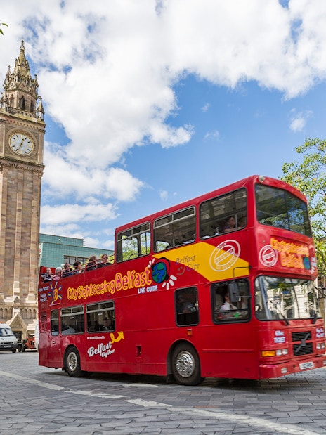 Red double-decker bus near Belfast's Albert Memorial Clock on sightseeing tour.