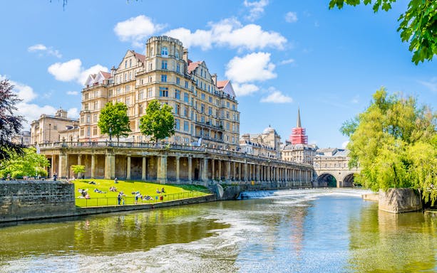 Pulteney Bridge over River Avon in Bath, England, with historic architecture and lush greenery.