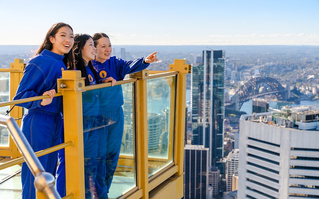 Visitors on Sydney Tower Eye Skywalk overlooking cityscape and Sydney Harbour Bridge.