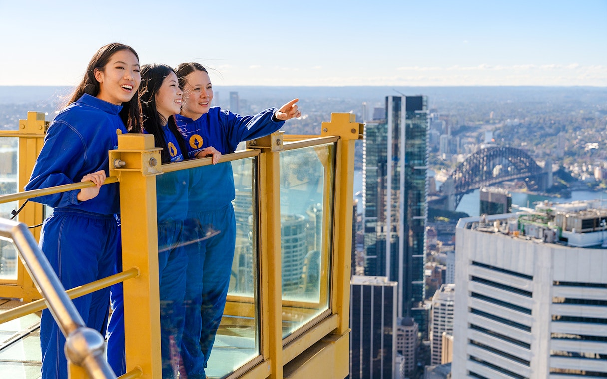 Visitors on Sydney Tower Eye Skywalk overlooking cityscape and Sydney Harbour Bridge.