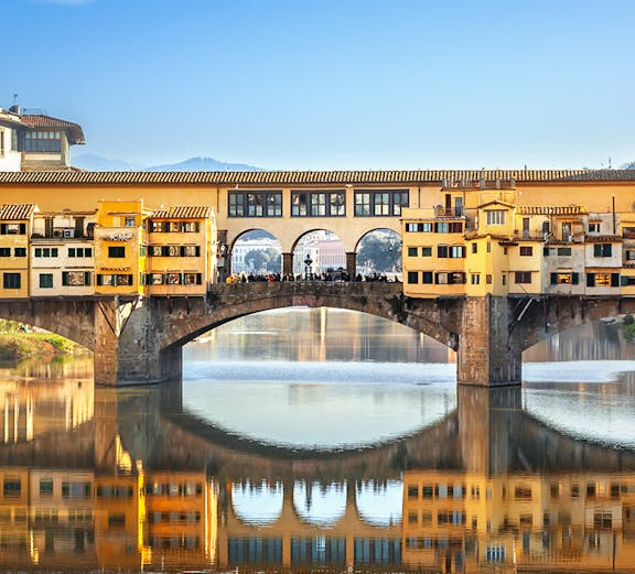Ponte Vecchio bridge over Arno River in Florence, Italy, reflecting in the water.