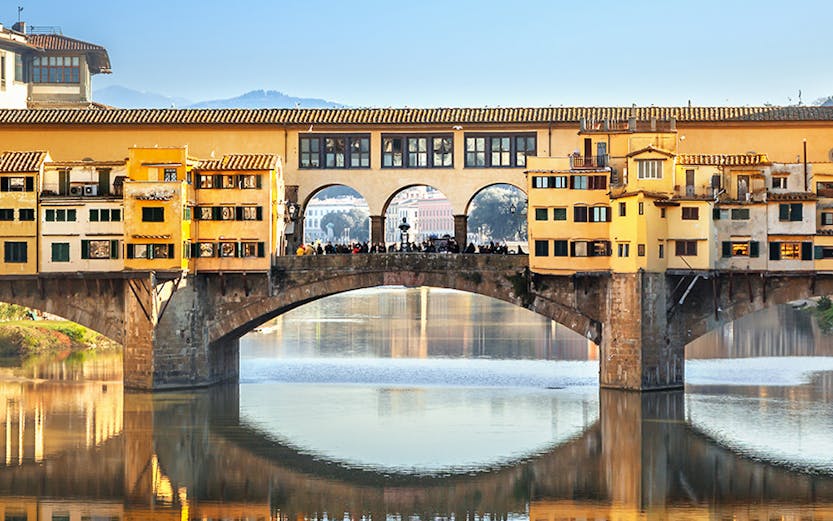 Ponte Vecchio bridge over Arno River in Florence, Italy, reflecting in the water.