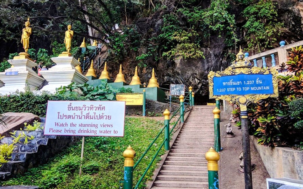 Stairs leading to Tiger Cave Temple in Krabi with golden statues and lush greenery.