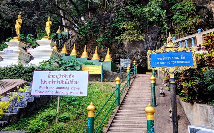 Stairs leading to Tiger Cave Temple in Krabi with golden statues and lush greenery.