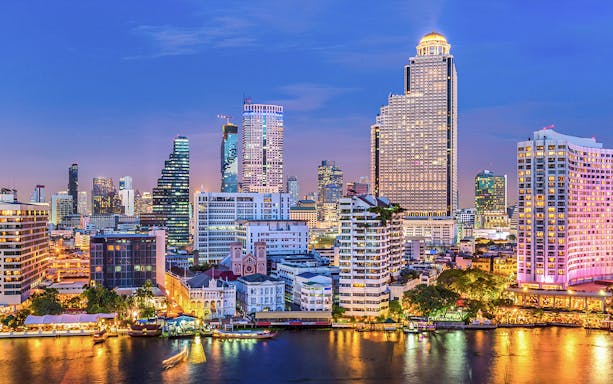 Bangkok skyline with Chao Phraya River in the foreground at dusk.