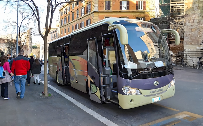Tourists boarding an AC coach vehicle on a city street.