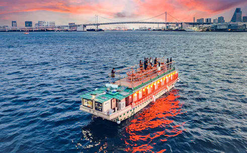 Tokyo dinner cruise with guests on deck, Rainbow Bridge in background during cherry blossom season.