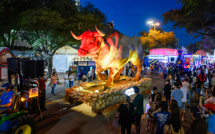 Giant illuminated bull float at State Fair of Texas parade with crowd watching.
