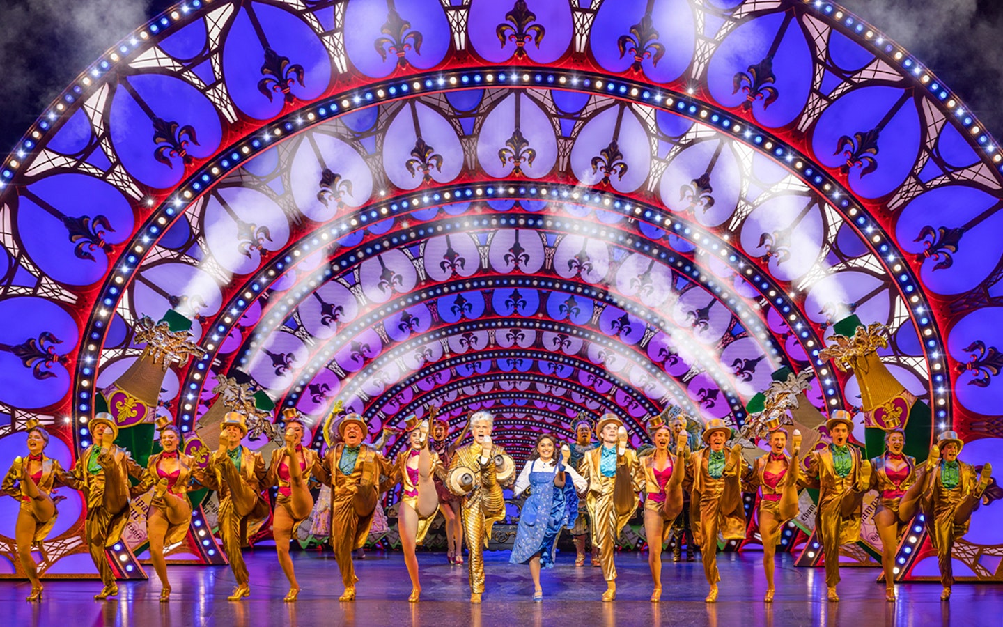 Performers in a "Beauty and the Beast" stage show with vibrant costumes and illuminated arches.