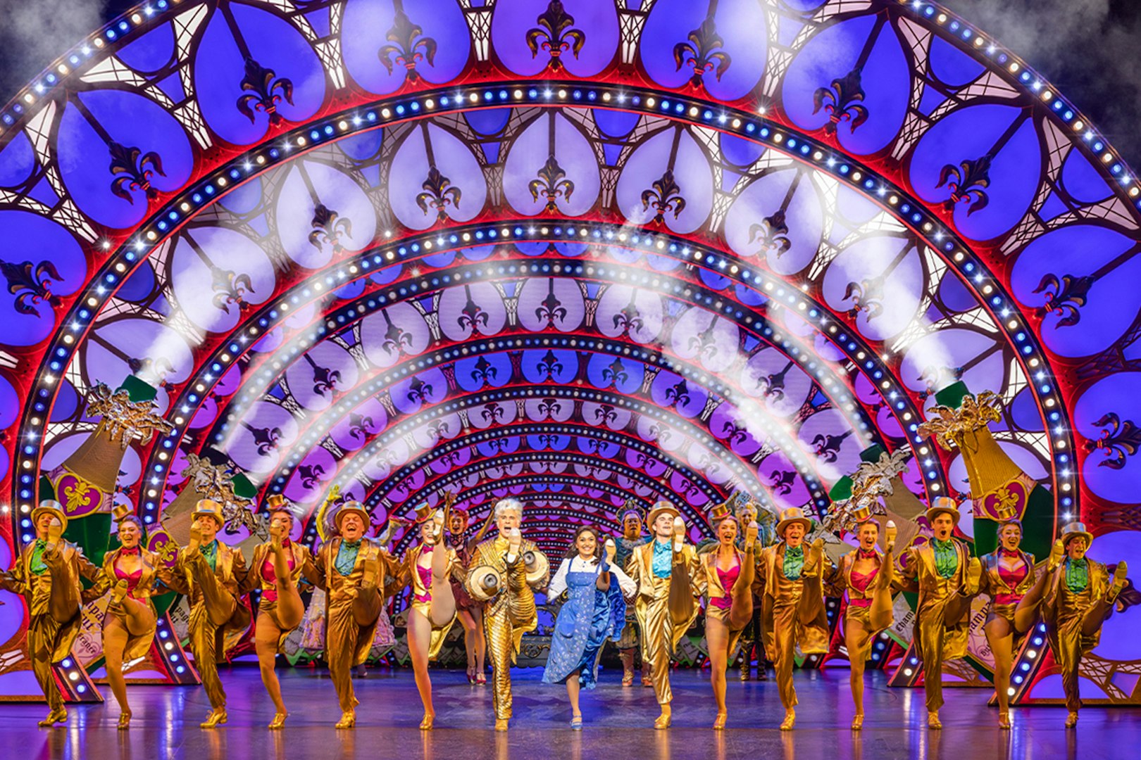 Performers in a "Beauty and the Beast" stage show with vibrant costumes and illuminated arches.