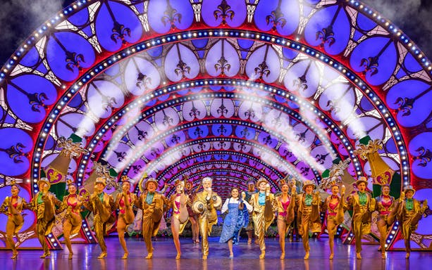 Performers in a "Beauty and the Beast" stage show with vibrant costumes and illuminated arches.