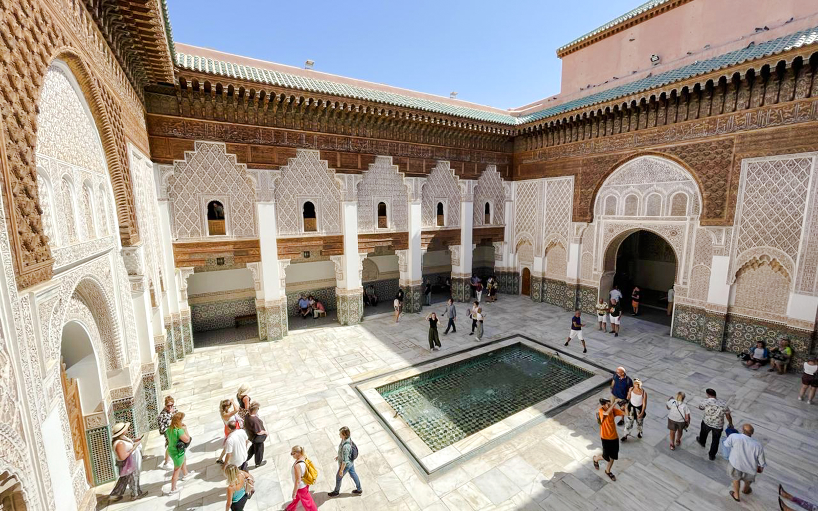 Ben Youssef Madrasa courtyard with intricate tilework and visitors in Marrakech, Morocco.
