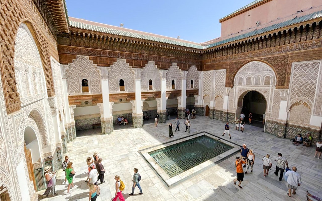 Ben Youssef Madrasa courtyard with intricate tilework and visitors in Marrakech, Morocco.