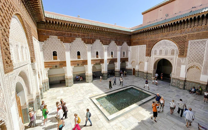 Ben Youssef Madrasa courtyard with intricate tilework and visitors in Marrakech, Morocco.