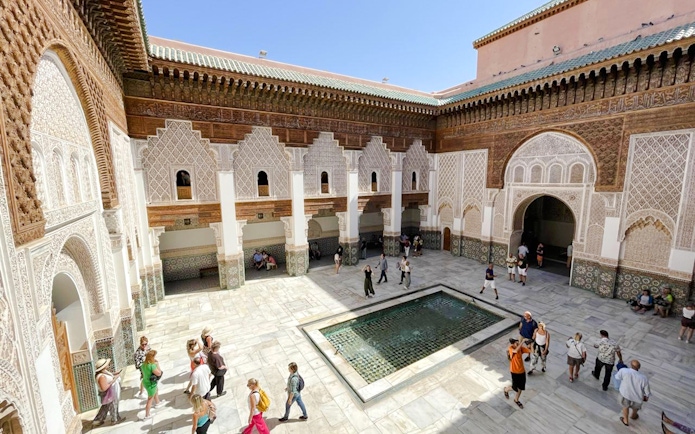 Ben Youssef Madrasa courtyard with intricate tilework and visitors in Marrakech, Morocco.
