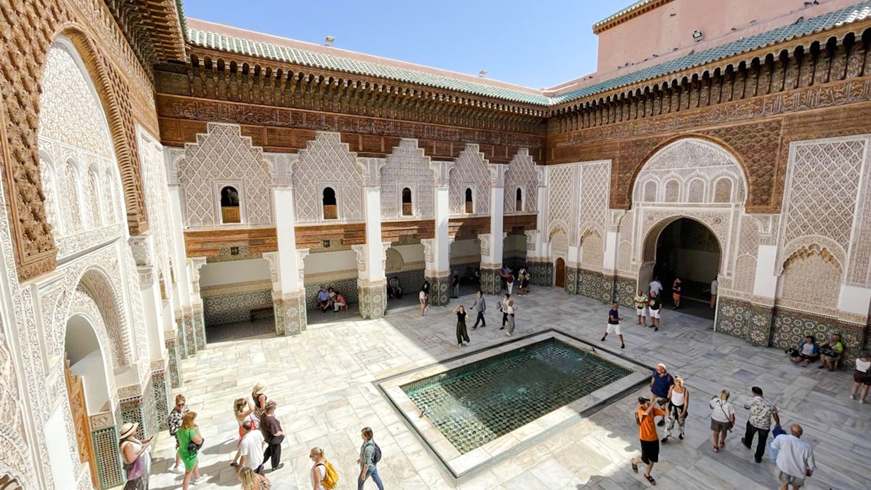 Ben Youssef Madrasa courtyard with intricate tilework and visitors in Marrakech, Morocco.