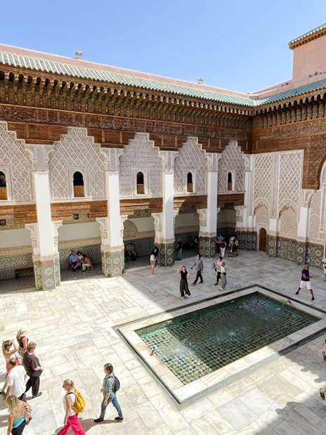 Ben Youssef Madrasa courtyard with intricate tilework and visitors in Marrakech, Morocco.