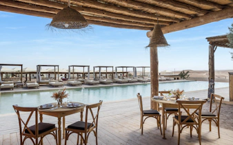 Outdoor dining area overlooking pool at Les Terrasses d'Agafay camp with desert views.