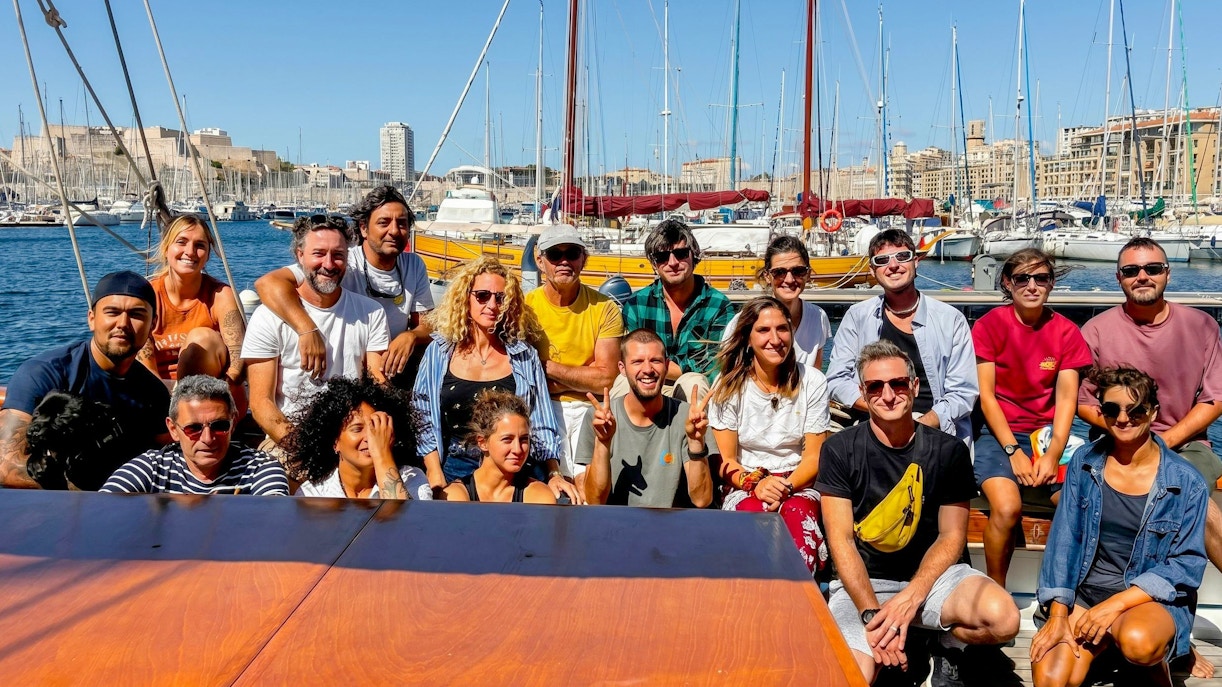 Group of people on a boat excursion in Calanques de Cassis, with marina and cityscape in the background.