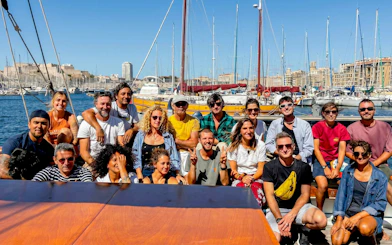 Group of people on a boat excursion in Calanques de Cassis, with marina and cityscape in the background.