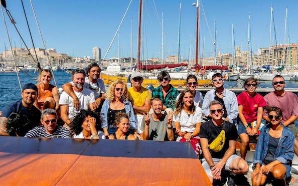 Group of people on a boat excursion in Calanques de Cassis, with marina and cityscape in the background.