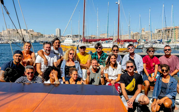 Group of people on a boat excursion in Calanques de Cassis, with marina and cityscape in the background.