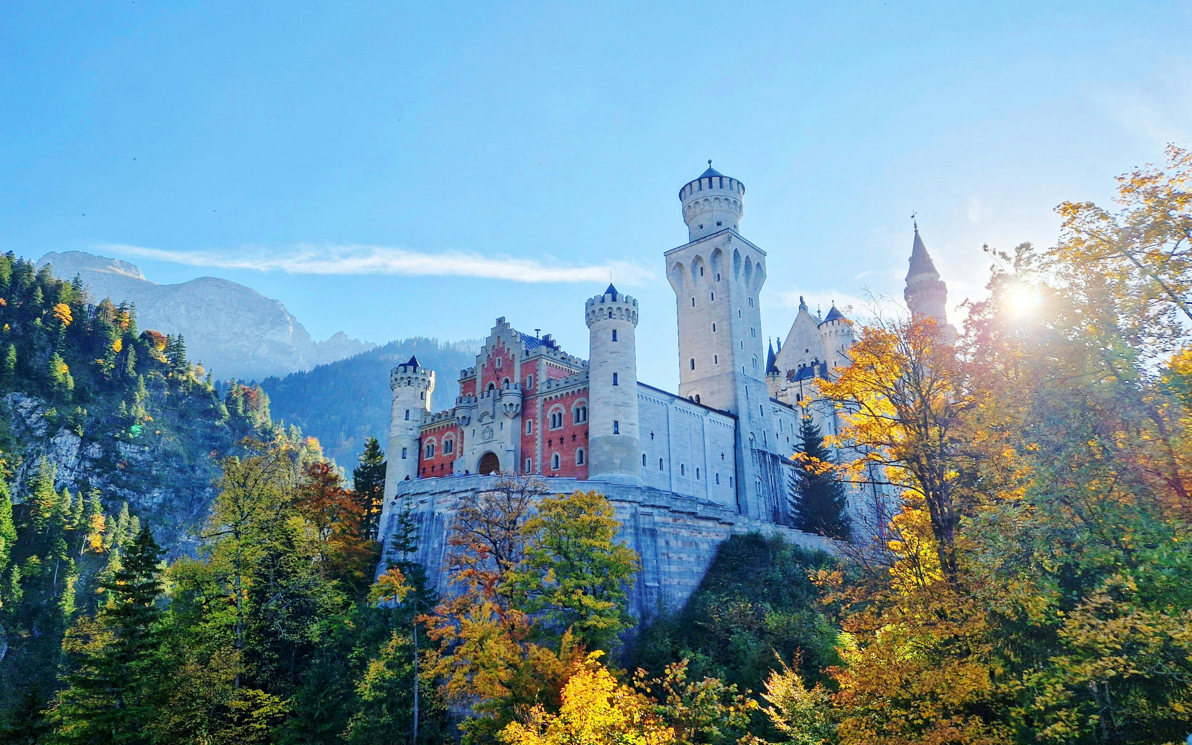 Neuschwanstein Castle in Bavaria surrounded by autumn trees and mountains.
