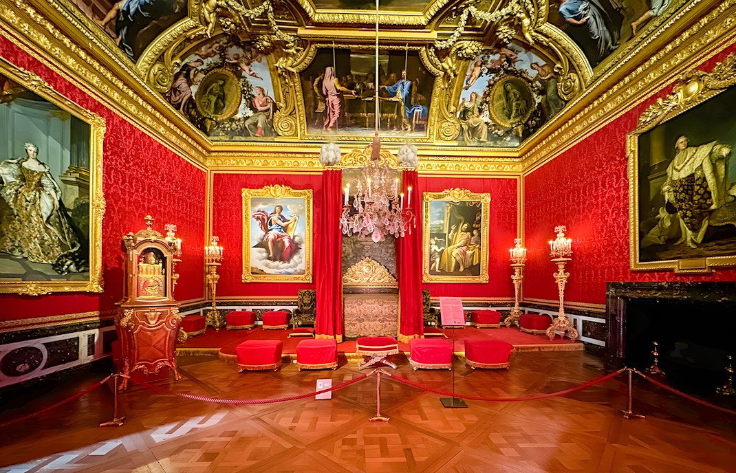 Palace of Versailles Royal Quarters interior with ornate red furnishings and detailed ceiling.