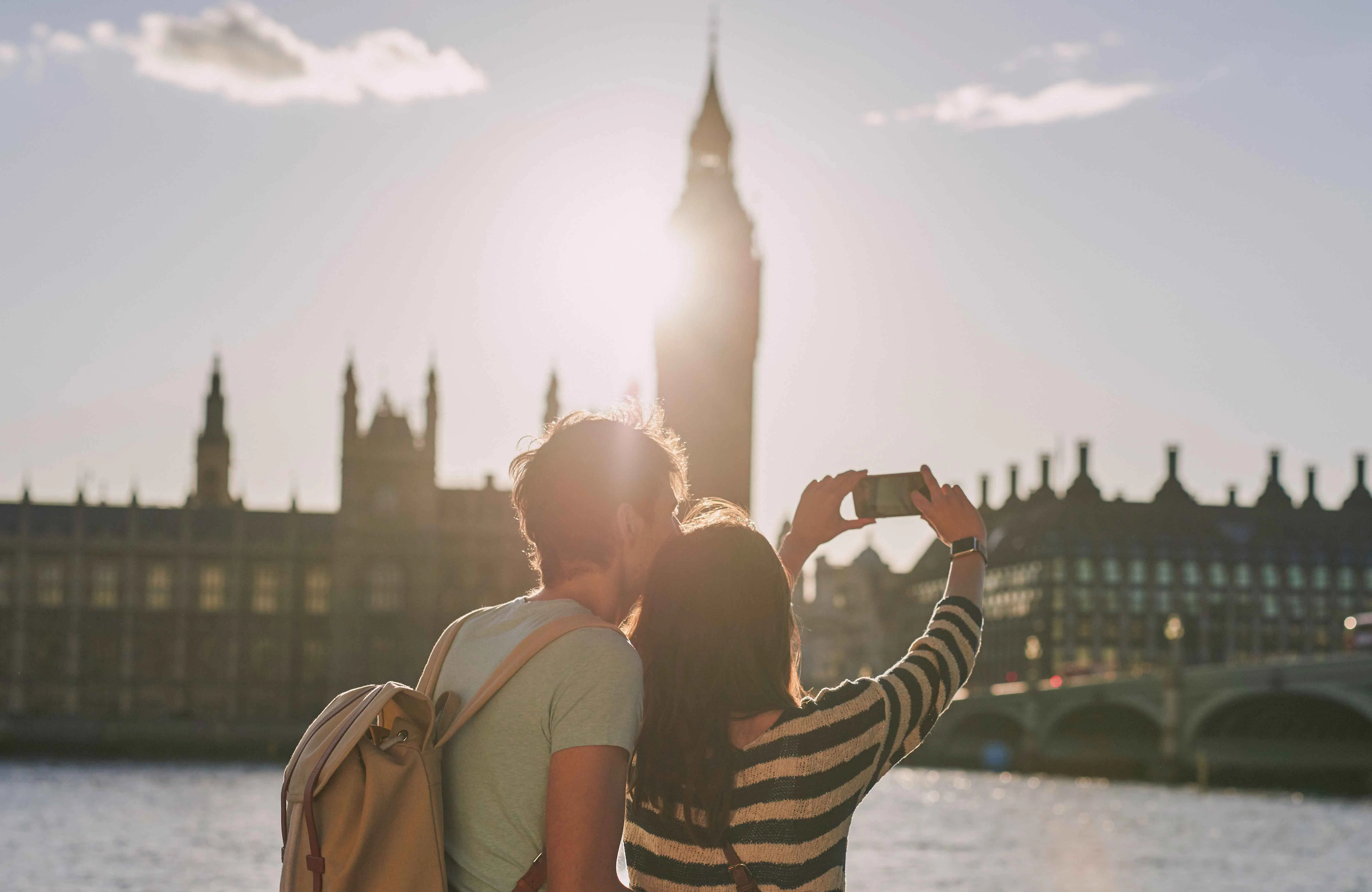 Couple taking selfie on Thames River cruise with Big Ben in background.