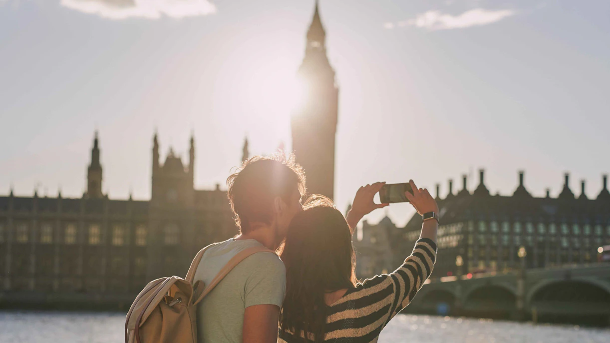 Couple taking selfie on Thames River cruise with Big Ben in background.