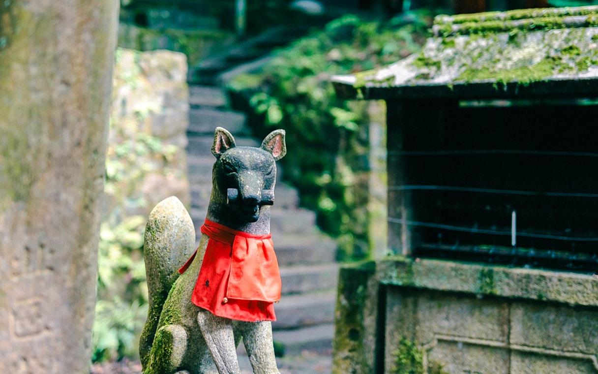 Stone fox statue with red bib at Fushimi Inari Taisha, Kyoto, Japan.