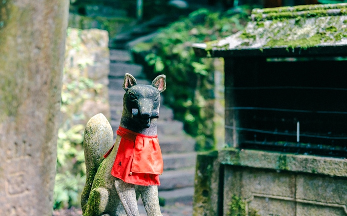Stone fox statue with red bib at Fushimi Inari Taisha, Kyoto, Japan.