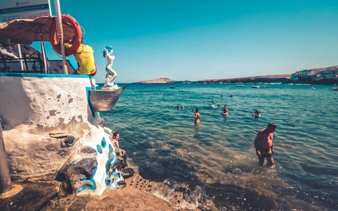 People swimming near a coastal sculpture in Gran Canaria during the Red Canyon Tour.