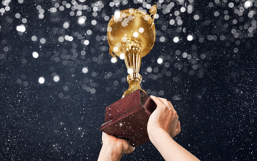 Hands holding a gold champions trophy against a sparkling background.