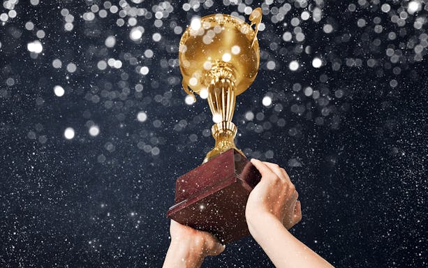Hands holding a gold champions trophy against a sparkling background.