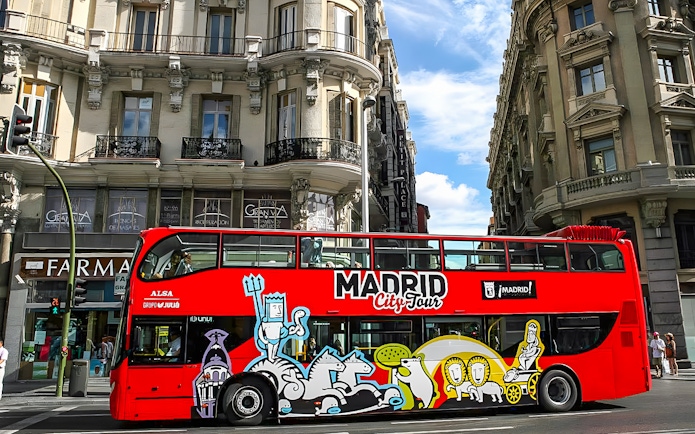 Red Madrid City Tour bus on a street with historic buildings in Madrid.