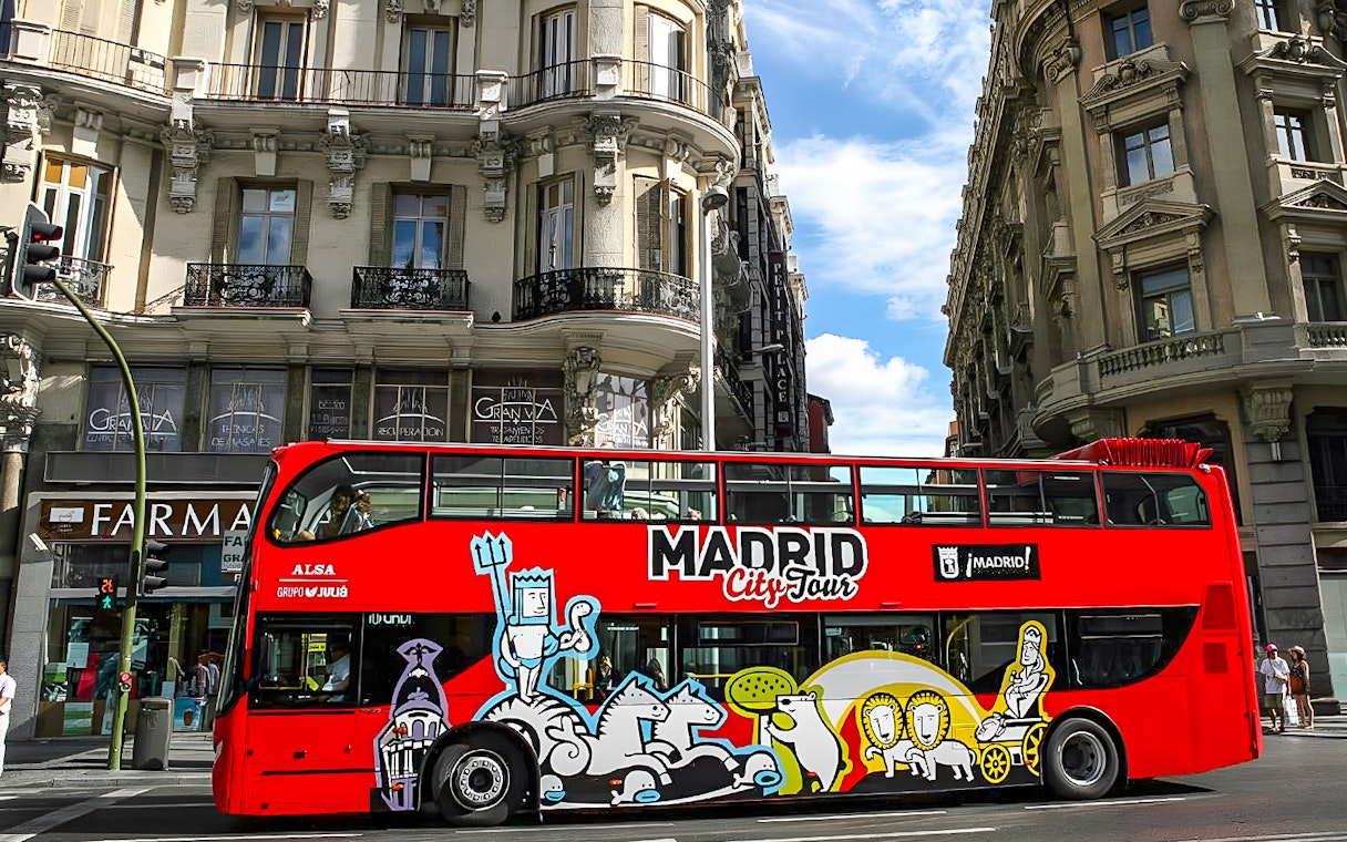 Red Madrid City Tour bus on a street with historic buildings in Madrid.