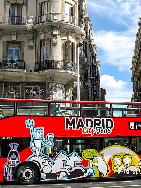 Red Madrid City Tour bus on a street with historic buildings in Madrid.